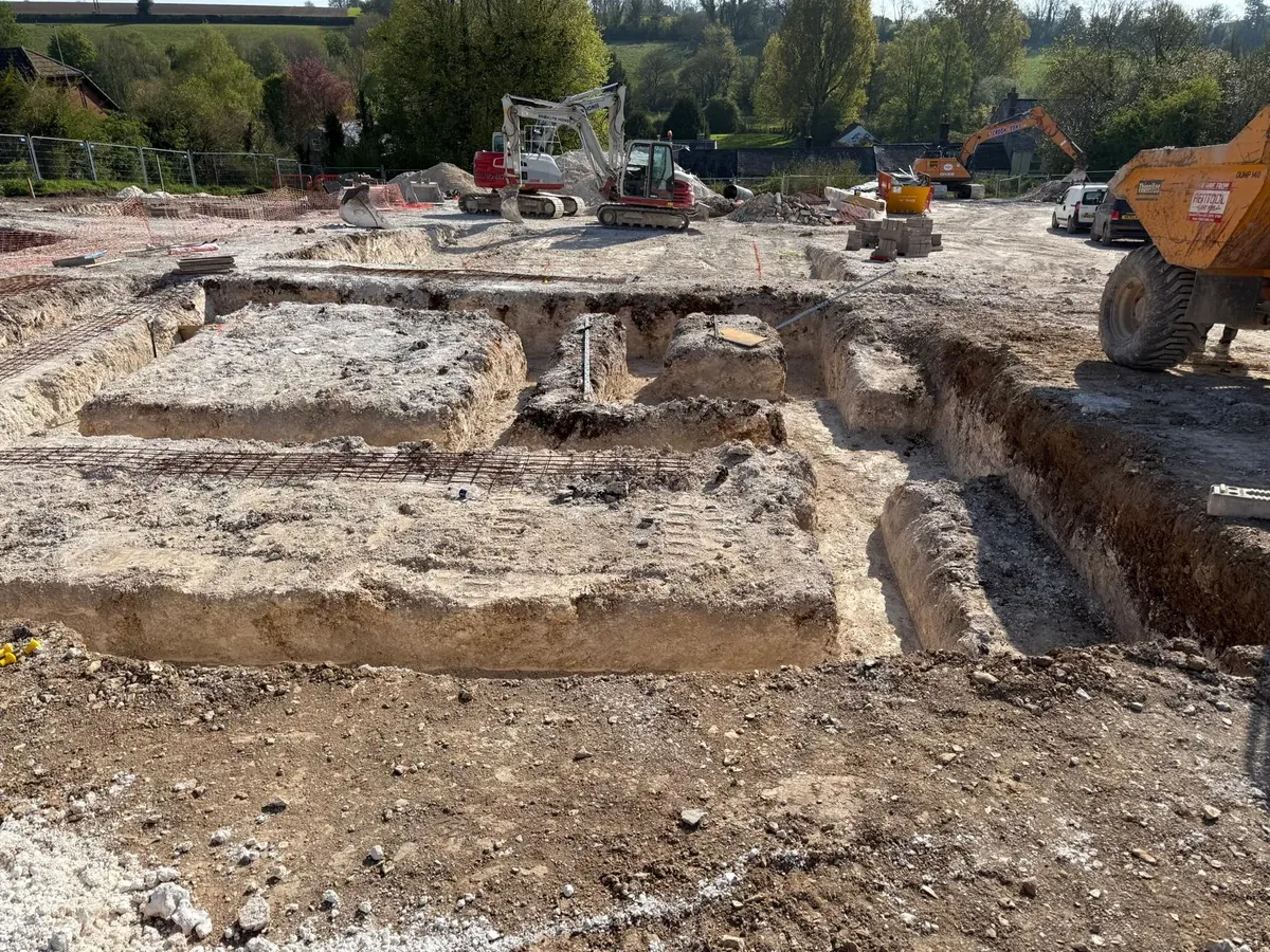 Excavated foundation trenches on a groundworks site with plant machinery